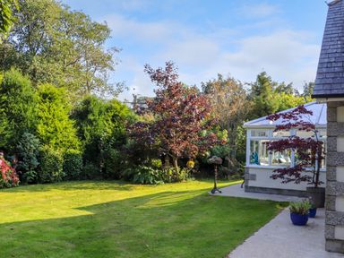 A garden with grass trees shrubs and a conservatory next to a house at Lower Gadles in Burnthouse near Falmouth