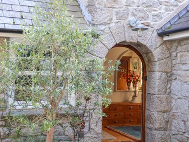 A stone doorway with an arched entrance revealing a wooden drawer chest and a vase with flowers at Lower Gadles Burnthouse near Falmouth