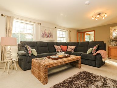 A living room with a dark grey sectional sofa and wicker coffee table at Lower Gadles in Burnthouse near Falmouth