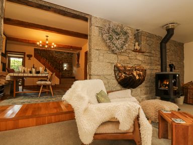 A living room with a wood burning stove a wooden chair with a white throw and a dining area with a table and chairs at Lower Gadles Burnthouse near Falmouth