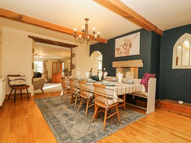 A dining room with a wooden table set for six chairs a bench and a chandelier at Lower Gadles Burnthouse near Falmouth