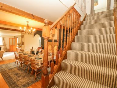 A dining area with a wooden table set for six and a striped carpeted staircase at Lower Gadles in Burnthouse near Falmouth