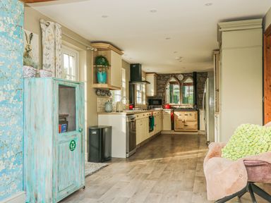 A kitchen with cream cabinets a recycled bin a beige oven and a pink chair at Lower Gadles in Burnthouse near Falmouth
