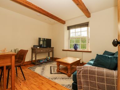 A living room with a wooden coffee table a blue sofa TV on a stand and a window at Lower Gadles in Burnthouse near Falmouth