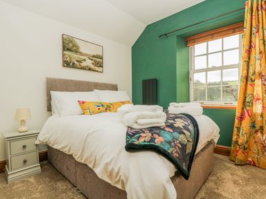 A bedroom with a bed bedside table lamp and window at Lower Gadles in Burnthouse near Falmouth