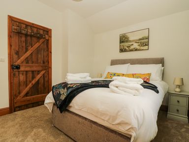 A bedroom with a wooden door a bed with white bedding and folded towels and a nightstand with a lamp at Lower Gadles Burnthouse near Falmouth