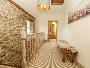 A hallway with stone wall window railing wooden bench and floral painting at Lower Gadles Burnthouse near Falmouth