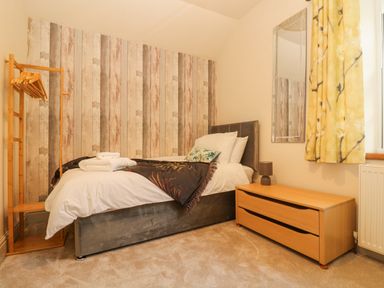 A bedroom with a single bed a wooden dresser with a lamp a standing clothes rack and a yellow curtain at Lower Gadles Burnthouse near Falmouth