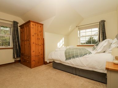 A bedroom with a bed covered with white bedding and a green blanket next to two windows and a wooden wardrobe at Lower Gadles Burnthouse near Falmouth