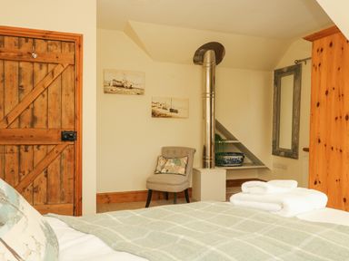 A bedroom with a wooden door a chair with a cushion a metal chimney and folded towels at Lower Gadles in Burnthouse near Falmouth