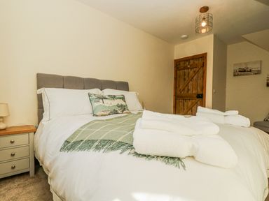 A bedroom with a bed white bedding and green throw a bedside table with lamp and wooden door at Lower Gadles Burnthouse near Falmouth