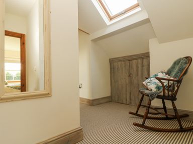 A hallway with a rocking chair, a wall mirror, a skylight, and wooden storage doors at Lower Gadles Burnthouse near Falmouth