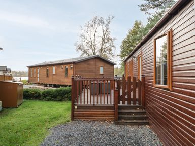 Two wooden lodges with fenced decks and grassy area in between at Wansfell Lodge Pony Meadow 36 White Cross Bay near Windermere