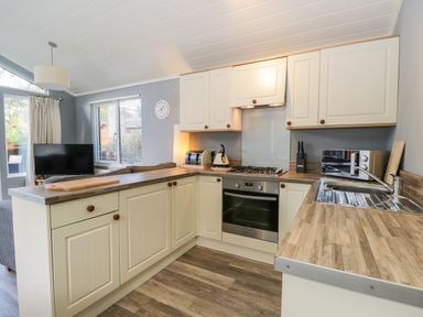 A kitchen with white cabinets a wooden countertop a gas stove a microwave and a sink at Wansfell Lodge in Pony Meadow 36 White Cross Bay near Windermere