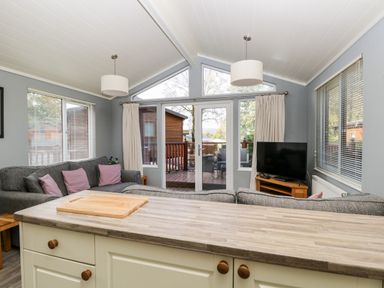 A living room with sofas a television and a kitchen counter with a cutting board at Wansfell Lodge Pony Meadow 36 White Cross Bay near Windermere