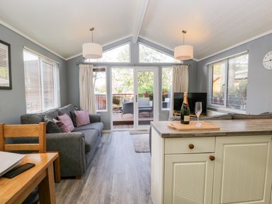 A living room with sofas a dining table kitchen island and glass doors leading to a deck deck furniture visible outside at Wansfell Lodge in Pony Meadow 36 White Cross Bay near Windermere