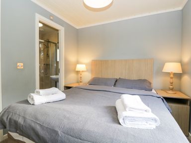 A bedroom with a bed towels on the bed two lamps on wooden nightstands and a bathroom visible through an open door at Wansfell Lodge Pony Meadow 36 White Cross Bay near Windermere