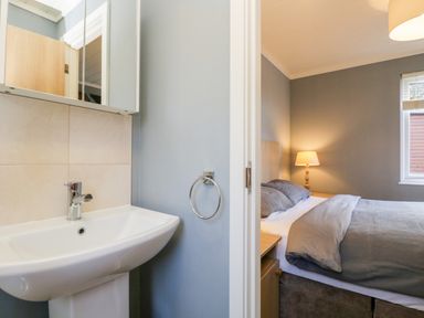 A bathroom sink with a mirror cabinet and a bedroom with a bed a lamp and a window at Wansfell Lodge Pony Meadow 36 White Cross Bay near Windermere