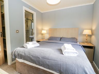 A bedroom with a bed with gray bedding two bedside tables with lamps and an en suite bathroom at Wansfell Lodge Pony Meadow 36 White Cross Bay near Windermere