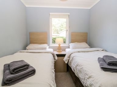 A bedroom with two single beds a bedside table with a lamp between them and a window behind at Wansfell Lodge Pony Meadow 36 White Cross Bay near Windermere