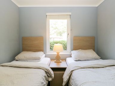 A bedroom with two single beds separated by a wooden nightstand and a lamp below a window at Wansfell Lodge in Pony Meadow 36 White Cross Bay near Windermere