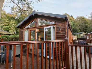 A wooden cabin with a deck and outdoor chairs at Wansfell Lodge Pony Meadow 36 White Cross Bay near Windermere
