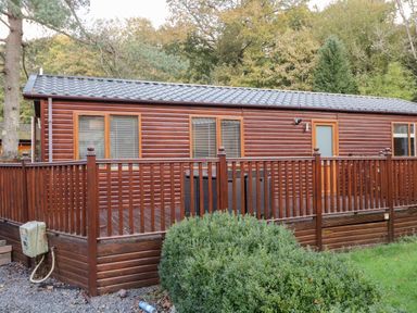 An exterior view of a wooden cabin with a fenced porch and green bushes in front at Wansfell Lodge in Pony Meadow 36 White Cross Bay near Windermere