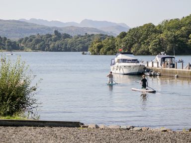 A lake with two people paddleboarding near boats and trees at Wansfell Lodge in Pony Meadow 36 White Cross Bay near Windermere