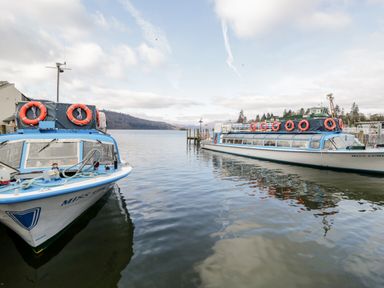 Two boats docked on a lake with a wooden pier and hills in the background at Wansfell Lodge in Pony Meadow 36 White Cross Bay near Windermere