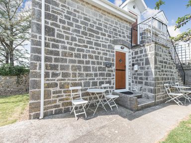 Exterior of a stone building with two white chairs and a table on each side of a wooden door at The Coach House in St Florence