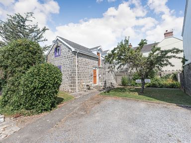 A stone building with wooden doors and purple trim surrounded by trees and grass with private parking signs at The Coach House in St Florence
