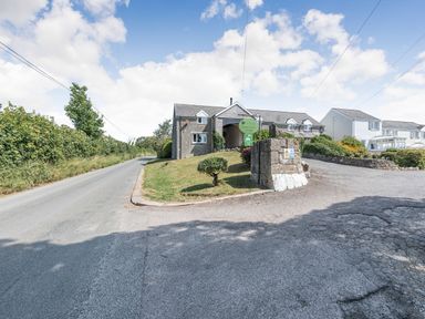 A paved road next to a grass lawn with a tree in front of a stone building with dormer windows and a sign at The Coach House in St Florence