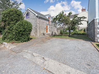 A gravel parking area with a stone building and garden with trees and chairs at The Coach House in St Florence