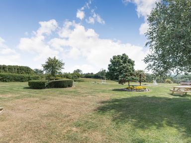 An open grassy area with trees bushes picnic tables and a partly cloudy sky at The Coach House in St Florence