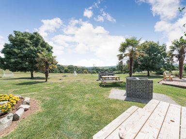 An outdoor area with picnic tables, brick barbecue grills, trees, and a flower bed at The Coach House in St Florence