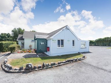 A small building with a fenced garden area and a parking lot surrounding it at The Coach House in St Florence