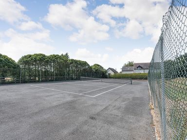 An outdoor tennis court surrounded by fencing and trees with houses in the background at The Coach House in St Florence