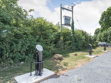 An outdoor area with electric vehicle charging stations near grass and bushes at The Coach House in St Florence