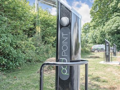 Electric vehicle charging points on grass with trees and a parked car in the background at The Coach House in St Florence