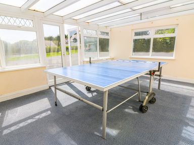 A sunroom with a table tennis table in the center and windows on all sides at The Coach House in St Florence