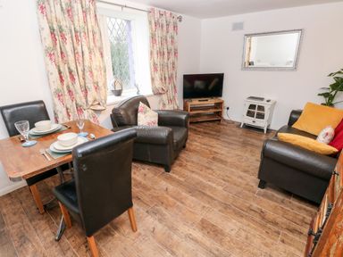 A living room with a dining table set for two armchairs a TV on a wooden stand and a sofa with cushions at The Coach House in St Florence
