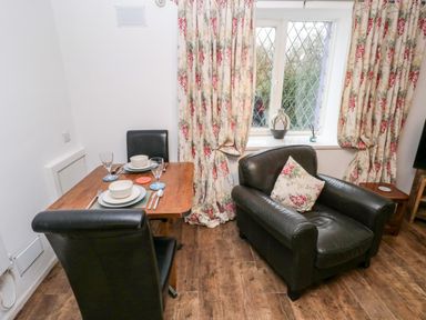 A dining table set for two with black chairs next to a black armchair and window with floral curtains at The Coach House in St Florence