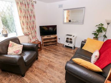A living room with leather armchairs a television on a wooden stand floral curtains and cushions at The Coach House in St Florence
