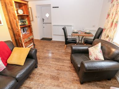 A living room with leather sofas, a wooden bookshelf, a small dining table with two chairs and place settings at The Coach House in St Florence
