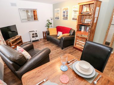 A living room with black leather sofas a wooden bookcase a television and a dining table with dishes at The Coach House in St Florence