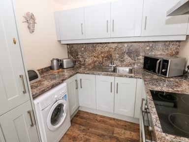A kitchen with white cabinets a washing machine a microwave kettle toaster and a sink at The Coach House in St Florence