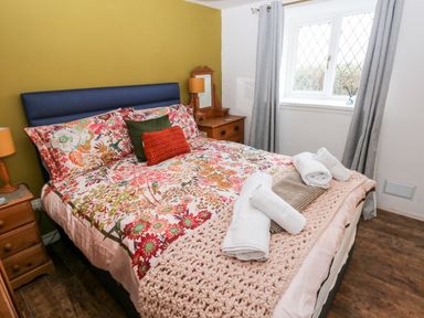 A bedroom with a double bed floral bedding bedside tables and window with curtains at The Coach House in St Florence