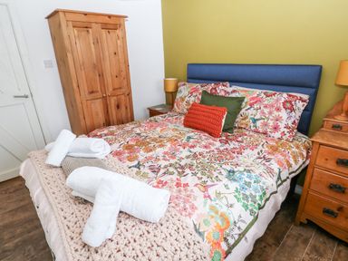 A bedroom with a bed covered in floral bedding and rolled towels on it next to wooden furniture at The Coach House in St Florence