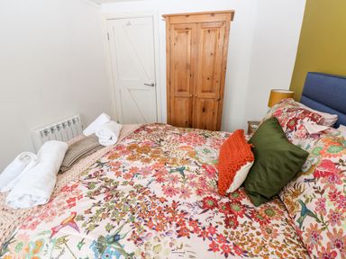 A bedroom with a bed covered in floral bedding pillows a wooden wardrobe and a door at The Coach House in St Florence
