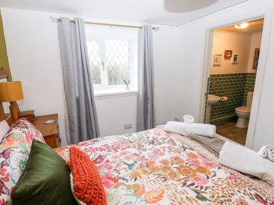 A bedroom with a floral bedspread green and orange pillows grey curtains and an ensuite bathroom at The Coach House in St Florence